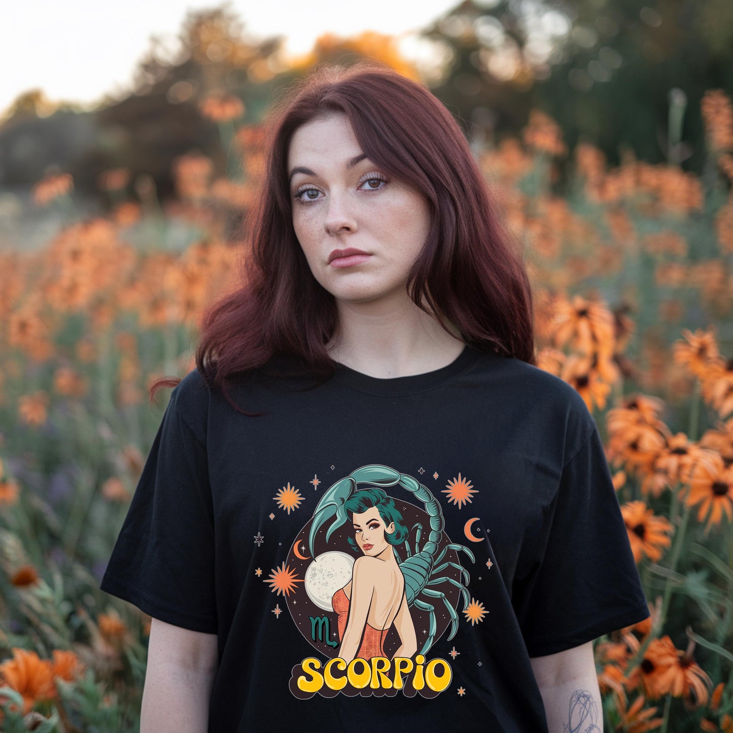 girl in field of flowers wearing a black vintage Scorpio zodiac t-shirt showcasing a classic distressed scorpion emblem. Horoscope apparel for November birthdays.